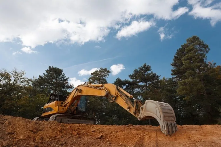 Clearing & Grubbing - Platinum Paving & Concrete A yellow excavator on the edge of a dirt hole.