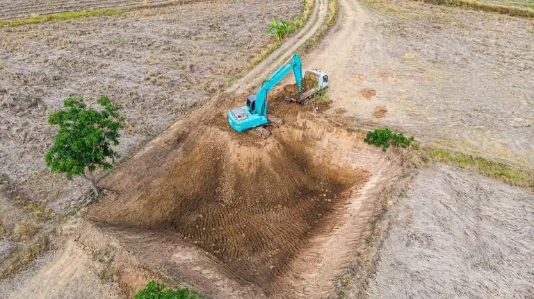 Clearing & Grubbing - Platinum Paving & Concrete A teal excavator working on a construction site.