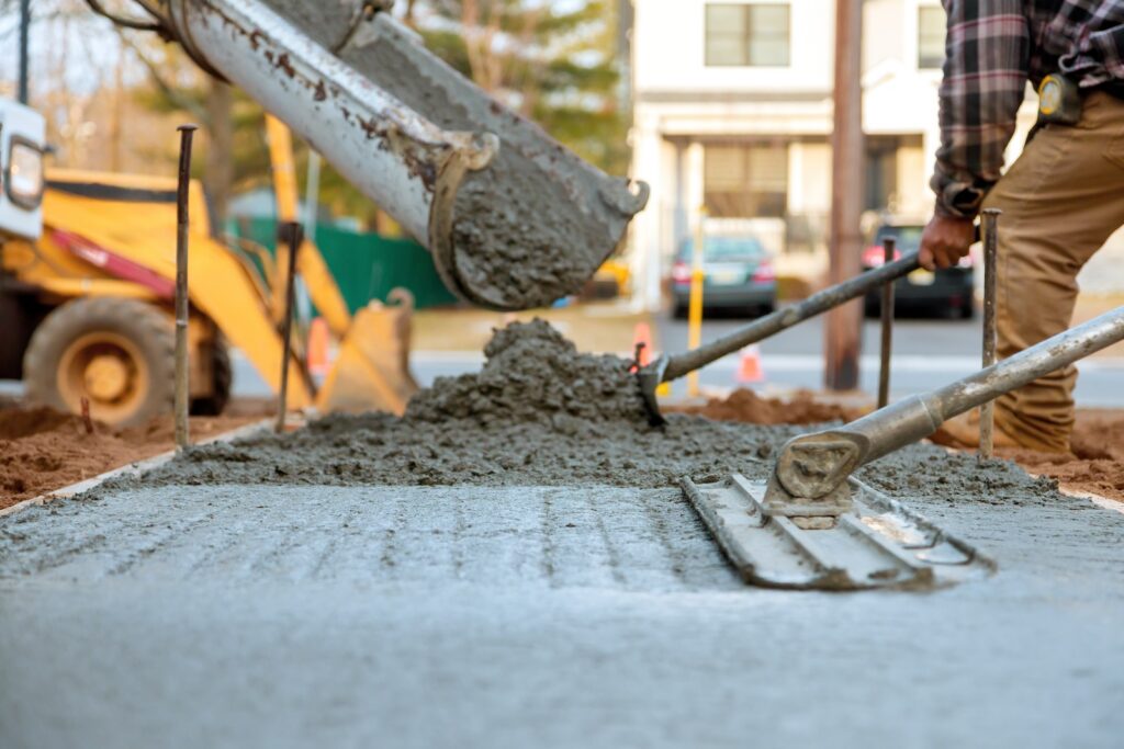 Workers pour, level fresh concrete for sidewalk amidst construction activities on works day