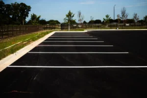 Freshly paved empty asphalt parking lot with white parking space markings