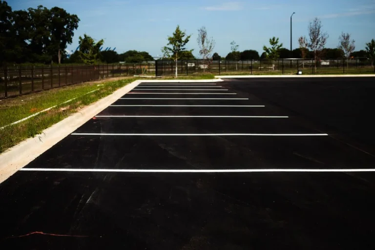 Freshly paved empty asphalt parking lot with white parking space markings