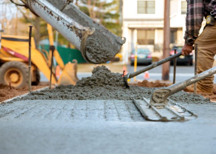 Workers pour, level fresh concrete for sidewalk amidst construction activities on works day