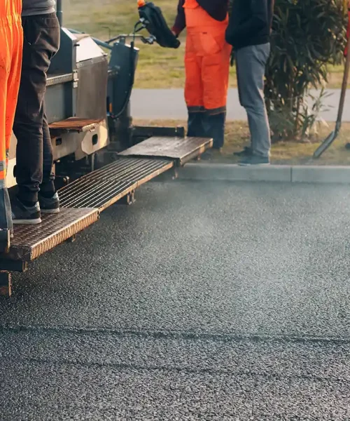 Workers use an asphalt paving machine.