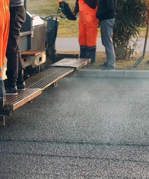Workers use an asphalt paving machine.