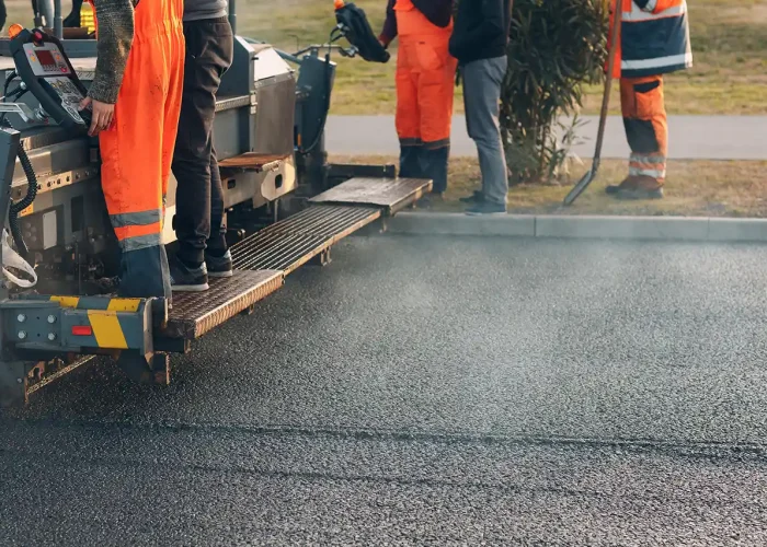 Workers use an asphalt paving machine.