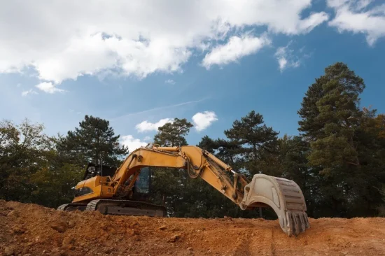 A yellow excavator on the edge of a dirt hole.