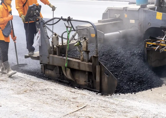 A machine pours hot asphalt onto the road.
