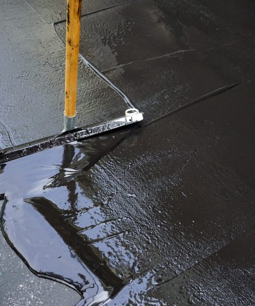 Man sealing asphalt driveway/Sealcoating selective focus