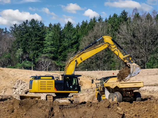 A yellow excavator dumps dirt into a flatbed.